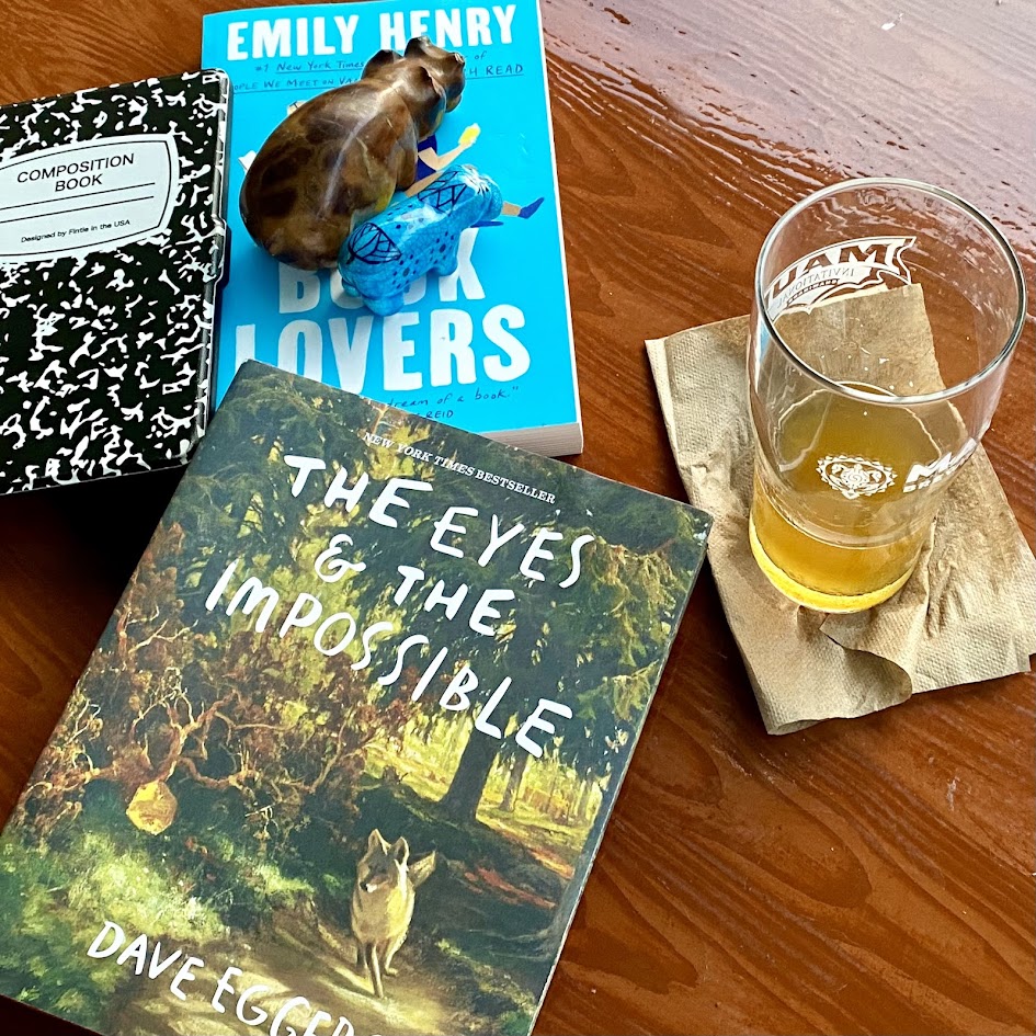 Two physical books and an Amazon Kindle next to a glass of beer and two  hippos.